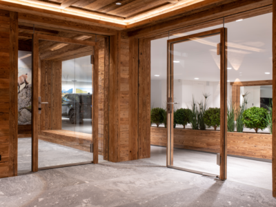 STURM zeigt einen Raum mit Holzverkleidung und Ganzglastüren mit silbernen Griffen und Sicht auf einen Gang mit Blumenkisten aus Holz.
