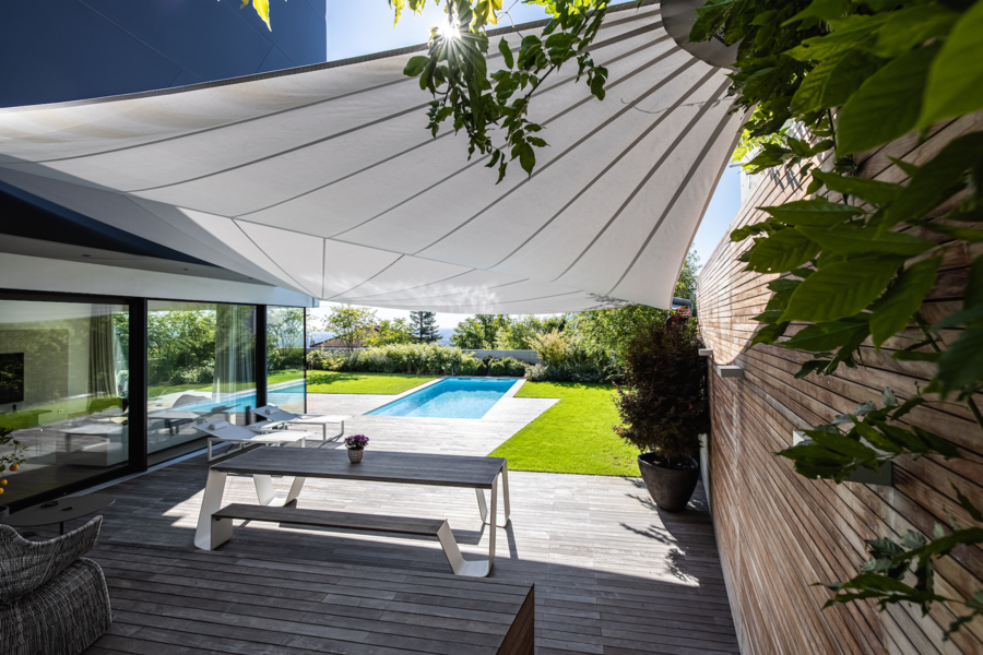 Beschattete Terrasse mit modernen Liegen und Picknickbank, die zum Verweilen einlädt. Das modische Sonnensegel kommt von SunSquare.