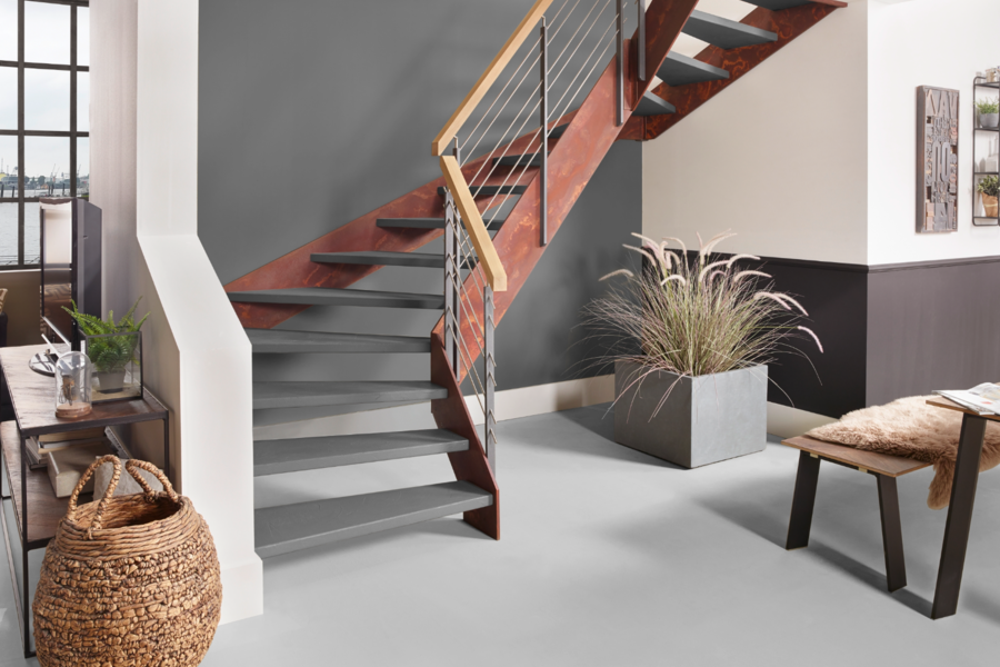 Treppenmeister zeigt ein Wohnzimmer mit akzentreicher Treppe bestehend aus grauen Stufen, einem Handlauf aus Holz und einem rostig anmutendem Gerüst, welches der Stiege ihren Industrial Look verleiht.