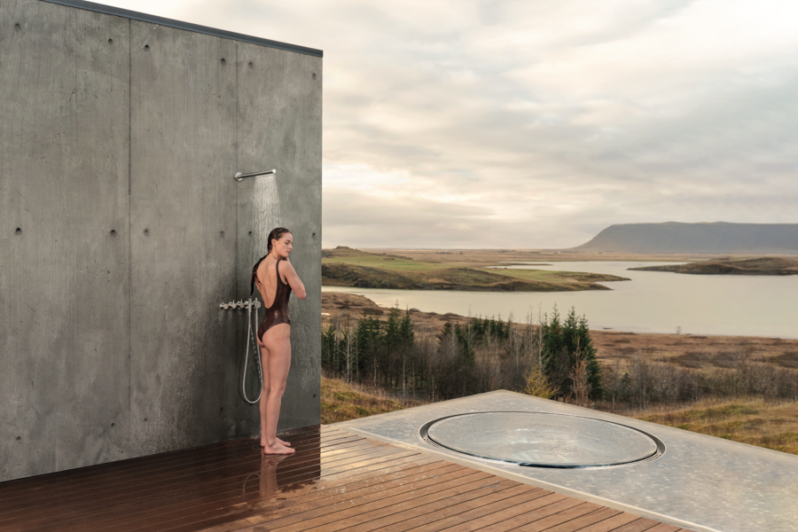 VOLA zeigt eine Outdoor-Dusche mit Regenfunktion an einer Betonwand mit silbernen Armaturen und Holzboden.