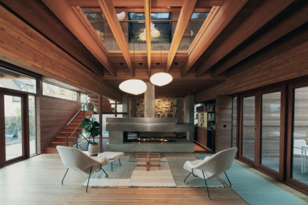Weissenseer Holz-System-Bau zeigt ein gemütliches Wohnzimmer in einem Holzhaus mit Loungesesseln, passenden Hockern und freiliegendem Teppich und mit Blick auf einen modernen Kamin.