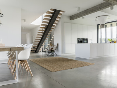 Moderne Innenarchitektur mit hochglänzender, griffloser Kücheninsel, freitragender Treppe und Esstisch.