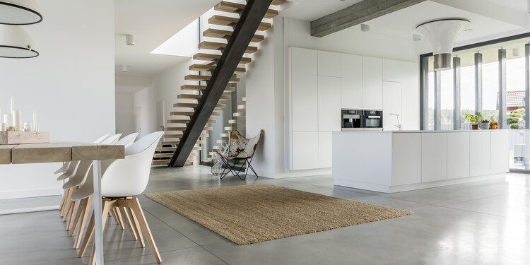 Moderne Innenarchitektur mit hochglänzender, griffloser Kücheninsel, freitragender Treppe und Esstisch.