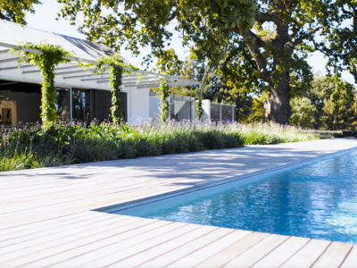Moderner Bungalow mit Pflanzenranken und großem, eckigem Pool mit hellen Terrassendielen aus Holz.