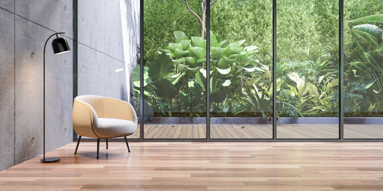 Lichtdurchfluteter Wohnraum mit modernem Wintergarten in hochformatiger Verglasung mit schwarzer Rahmeneinfassung mit Aussicht in den grünen Garten sowie Parkettboden aus Holz.