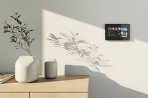 ABB zeigt eine Busch-Jaeger Steuereinheit mit großem Display in schwarz an einer weißen Wand in einem Wohnraum.