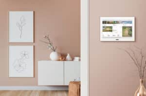 ABB zeigt eine Busch-Jaeger Steuereinheit mit großem Display in weiß an einer beigen Wand in einem Wohnraum.