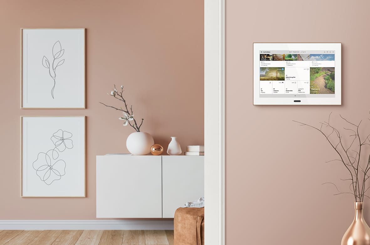 ABB zeigt eine Busch-Jaeger Steuereinheit mit großem Display in weiß an einer beigen Wand in einem Wohnraum.