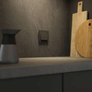 ABB zeigt einen Busch-Jaeger Schalter mit brauner Wippe und schiefergrauem Rahmen in Steinoptik in einer Küche.