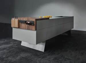 Eine graue Kochinsel mit diagonal verlaufenden Standbeinen und einer integrierten Holzarbeitsfläche mit Messerblock und anderen praktischen Halterungen von ALPHAOMEGA.