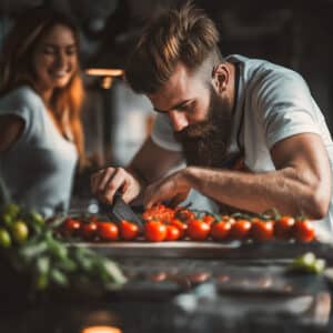 Ein bärtiger Mann schneidet Tomaten, während eine lachende Frau danebensteht in einer Familienküche von ALPHAOMEGA.
