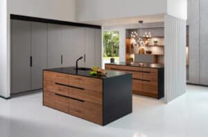 Eine Küche mit grauer Küchenzeile und zwei Kochinseln mit schwarzer Arbeitsplatte und Seitenwänden mit Fronten aus Nussbaumholz von ALPHAOMEGA.