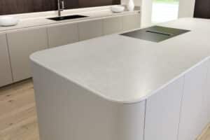 Eine grifflos gestaltete Küche mit abgerundeter, grauer Kochinsel, integriertem Kochfeld und Downdraft‑Dunstabzug von ALPHAOMEGA.