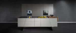 Eine moderne Küche in Grau mit glatter Front, Kochinsel aus Edelstahl mit schwarzer Arbeitsplatte, diagonal verlaufenden Schubladen und Standbeinen von ALPHAOMEGA.