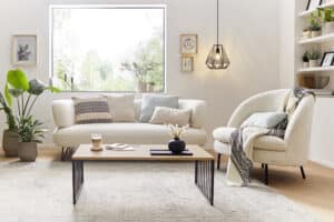 Ein heller Raum mit großem Fenster, gemütlichen Creme-Sofas und einem Holz-Couchtisch mit schwarzen Metallbeinen von ALPHAOMEGA.