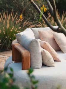 ALURE Outdoorliving zeigt eine gemütliche Outdoor-Couch mit Teakholz-Lehnen und weicher Polsterung mit grauem und beigem Stoffbezug.