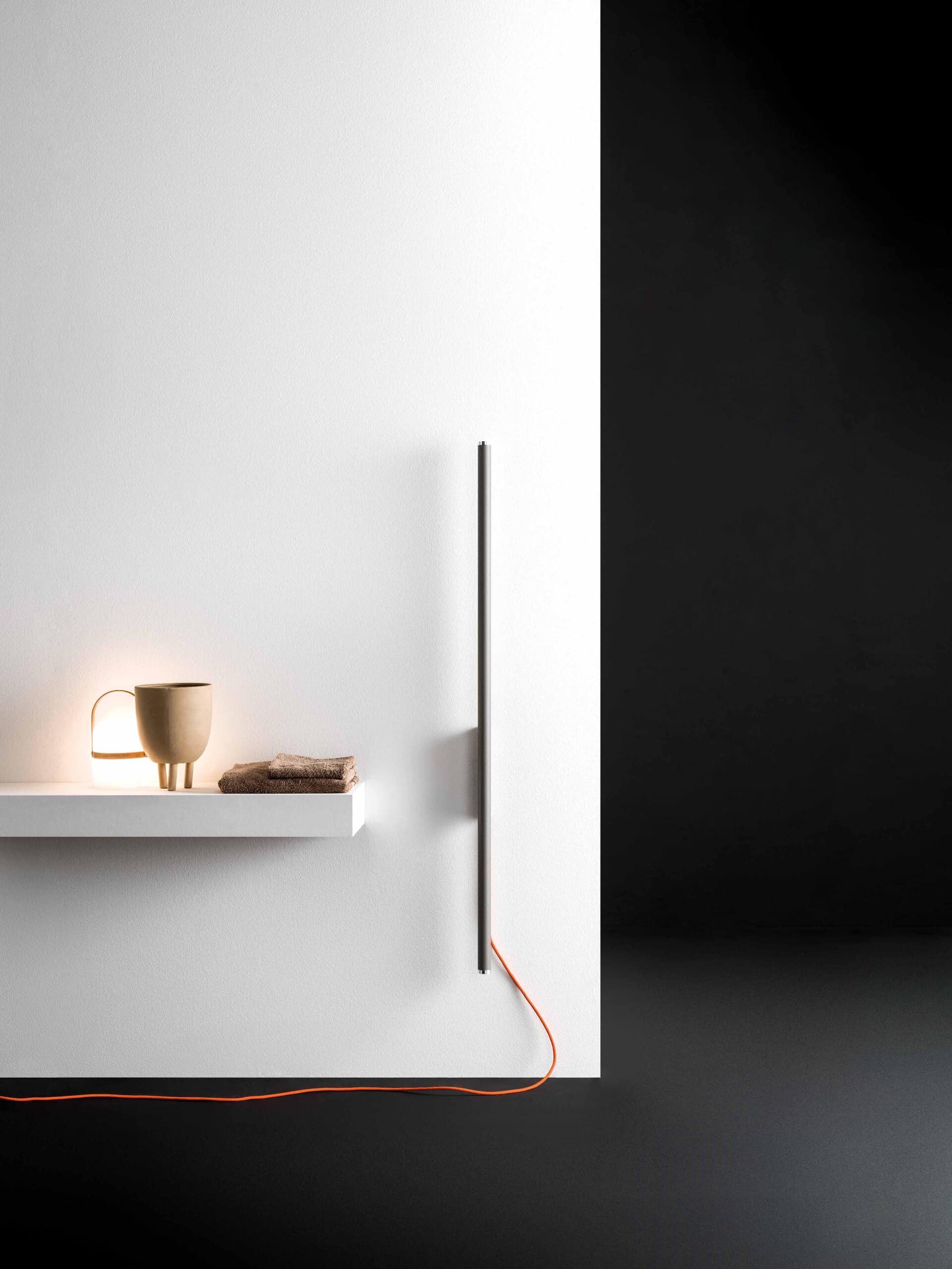 Nahaufnahme eines wandmontierten senkrechten Handtuchwärmers "Carlo & Tina" im silbernen Röhren-Look mit orangenem Stromkabel von ANTRAX IT.