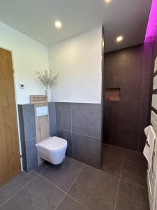 Badezimmer mit großformatigen grauen Fliesen, Duschnische, wandhängender Toilette, Handtuchwärmer und herabgesetzter Decke mit Spots und LED-Licht von der Bad Profi Salzburg Stadt.