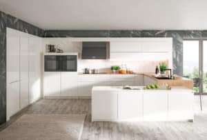Moderne grifflose weisse Küche mit heller Holzarbeitsfläche und Seitenteil und einer zentralen, aus ergonomischen Gründen niedrigeren Kücheninsel von DAN Küchen gezeigt von Salzburger Bad & Wohnraum.