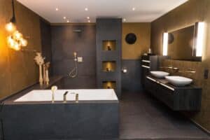 Elegantes Badezimmer mit schwarzen und anthrazitfarbenen Oberflächen und goldenen Akzenten und Armaturen von ELEMENTS gezeigt von Salzburger Bad & Wohnraum.