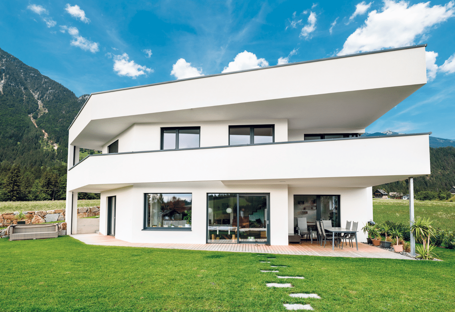 Bad Zeller zeigt ein einstöckiges Haus mit schrägen Hausecken, einer überdachten Terrasse mit Gartenmöbel darauf.