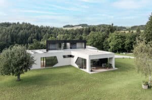 Modernes Wohnhaus mit Flachdach, dunkler Holzfassade im Obergeschoss, Dachterrasse, Balkon, großen Fenstern und geometrischen Glaselementen eingebettet in eine ruhige, grüne Landschaft, harmonisch von Bad Zeller.