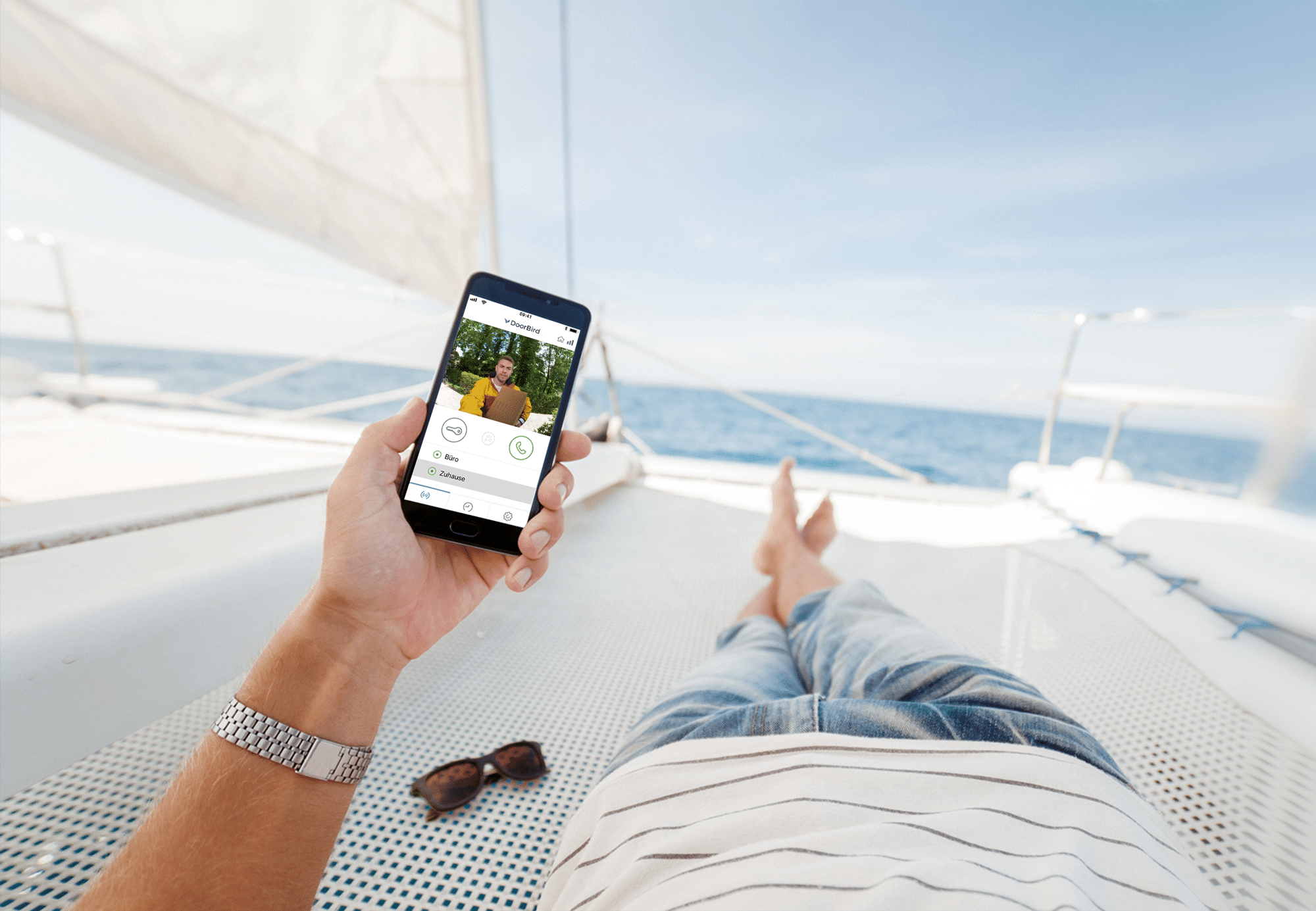 Bird Home Automation zeigt einen Mann auf einem Segelboot der per App auf seinem Smartphone seine Türsprechanlage zu Hause überwachen kann.