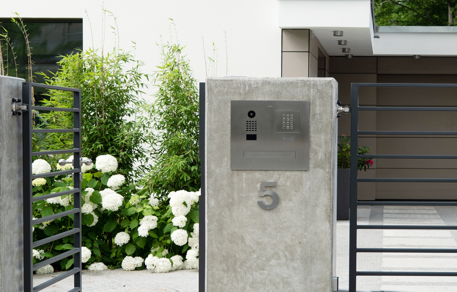 Bird Home Automation zeigt eine Türsprechanlage mit Videofunktion, Keypad und Postfach aus gebürstetem Edelstahl vor einem Einfamilienhaus.
