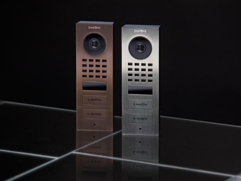 Bird Home Automation zeigt eine Türsprechanlage mit Videofunktion, Lautsprecher und zwei Namensschildern aus gebürstetem Edelstahl in Silber und Kupfer.