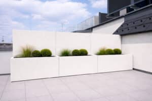 Drei lange, rechteckige Pflanzkübelelemente mit hoher Rückwand die als Sichtschutz dient in Warmweiss-Beige auf einer geräumigen Dachterrasse von Blumentrog-Flexi.