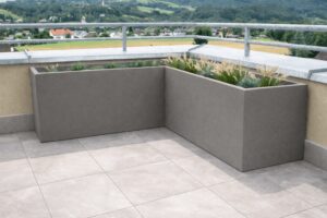 Eine Dachterrasse mit einem bepflanzten, hohen schlammfarbenen Pflanzkübel mit Hartschaumkern in L-Form von Blumentrog-Flexi.