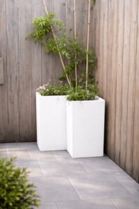 Eine Terrasse mit Sichtschutzzaun und einem hohen modernen weißen Ecktrog mit Bambus von Blumentrog-Flexi.