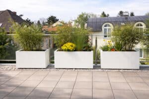 Blumentrog Flexi zeigt drei rechteckige Pflanzkübel im Flexi Design auf einer Dachterrasse als winterfeste weisse Outdoor-Blumenkästen.