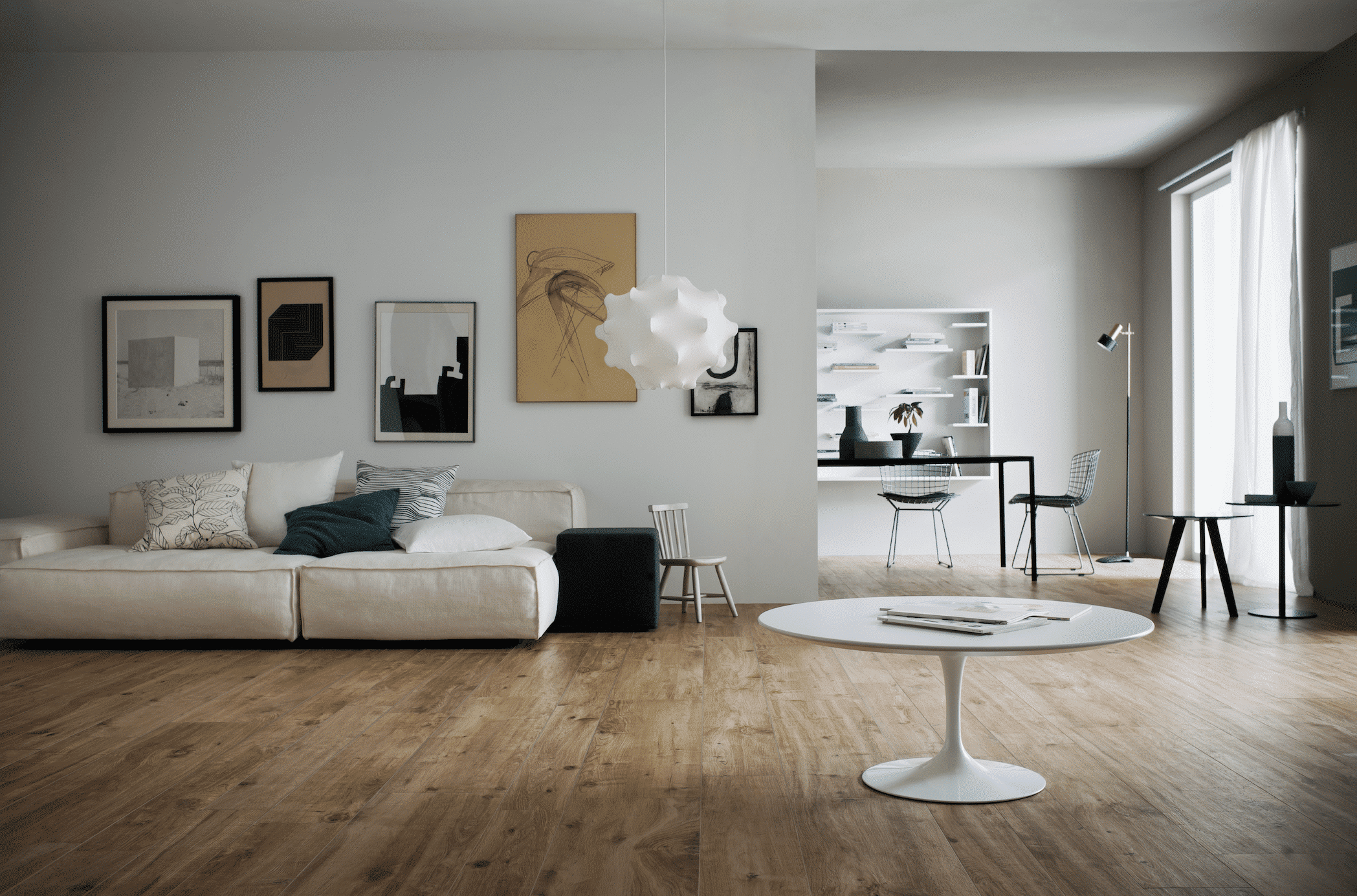 C. Bergmann zeigt ein Wohnzimmer mit Holzdielen, einem cremefarbenem Sofa mit Kissen und einen weissen, runden Beistelltisch mit Zugang zum Essbereich von Marazzi.