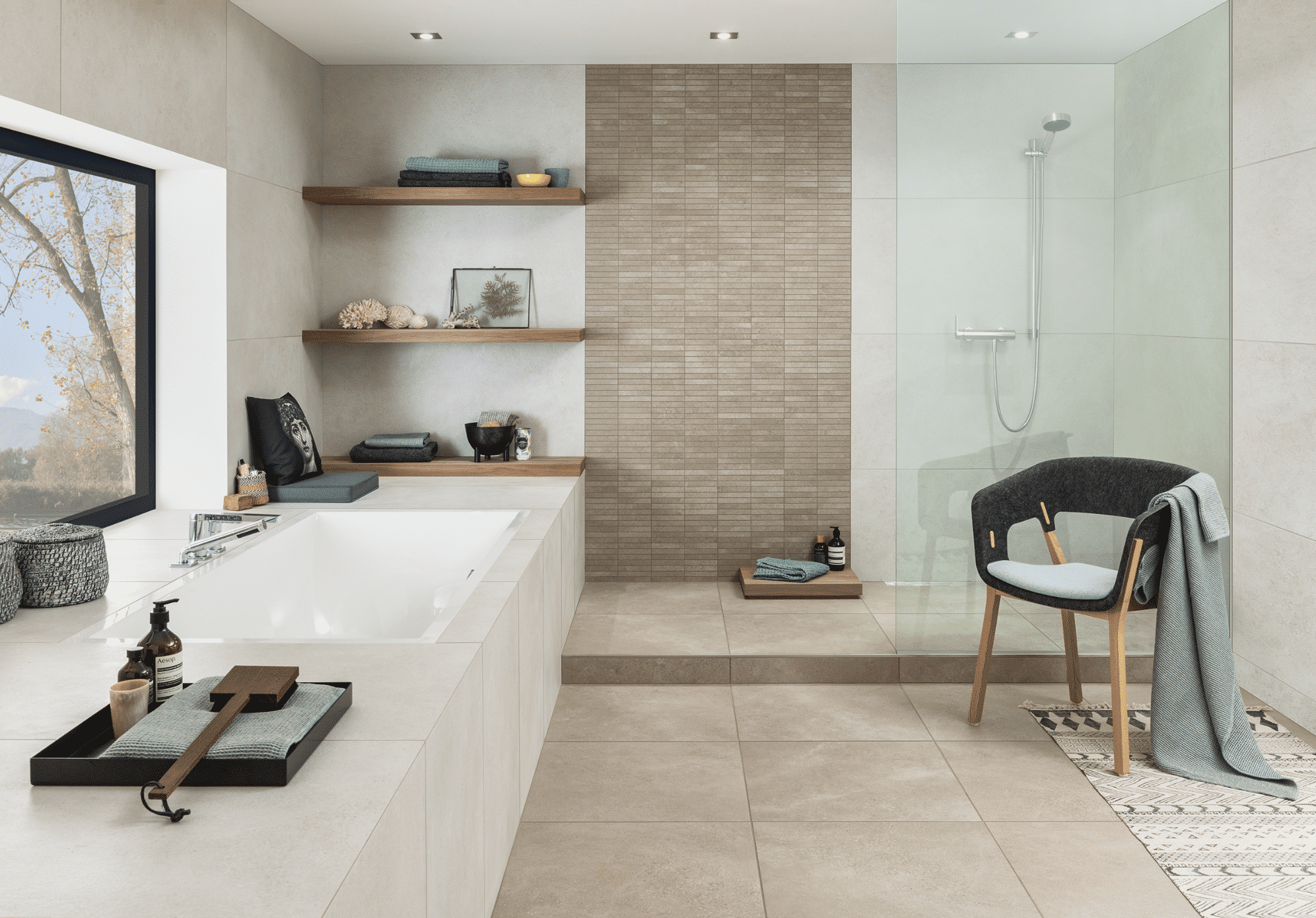 C. Bergmann zeigt ein hell gefliestes Badezimmer mit weissem Waschtisch,  Wandboards aus Holz und einer offenen Dusche mit silberner Armatur und Glaswand von Villeroy and Boch.