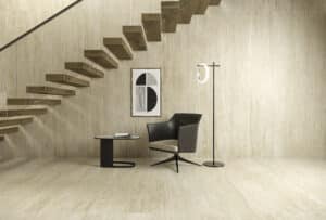 C.Bergmann zeigt einen offenen Wohnraum unterhalb eines Stiegenaufgangs mit beige marmorierten Wand- und Bodenfliesen von Atlas Concorde der Serie Marvel Travertine.