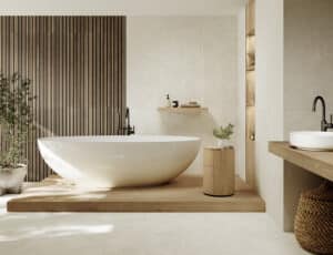 C.Bergmann zeigt ein helles Badezimmer mit einer freistehenden Badewanne auf einem Holzpodest und rechteckigen beige marmorierten Boden- und Wandfliesen von Grespania.