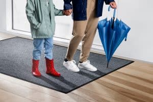 Mutter mit Kind in Regenbekleidung auf einer Schmutzfangmatte von CWS.