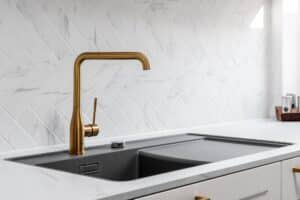 Landhausküche „Classico“ mit Kassettentüren in Weiß, goldenen Griffen, Arbeitsplatte in weißer Marmoroptik und goldenem Wasserhahn bzw. Mischbatterie von DANKÜCHEN.