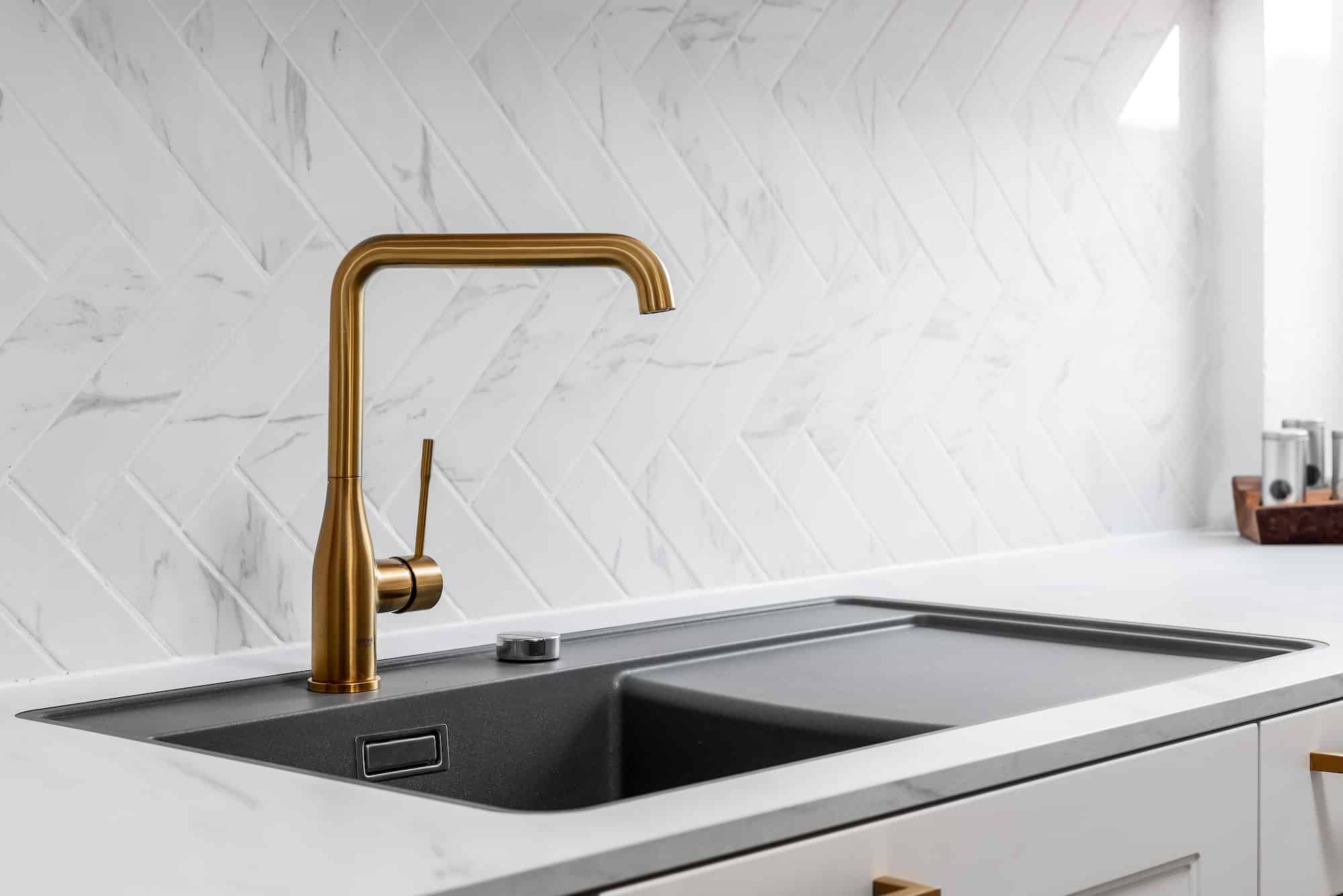 Landhausküche „Classico“ mit Kassettentüren in Weiß, goldenen Griffen, Arbeitsplatte in weißer Marmoroptik und goldenem Wasserhahn bzw. Mischbatterie von DANKÜCHEN.