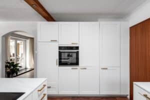 Landhausküche „Classico“ mit Kassettentüren in Weiß, goldenen Griffen, Arbeitsplatte in weißer Marmoroptik und wandbündig eingebauter Gerätezeile von DANKÜCHEN.