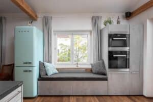 Küche „La Corte“ mit Gerätezeile, Sitzfenster und freistehendem Kühlschrank in Türkis, Fronten in Betonoptik und viel Stauraum von DANKÜCHEN.