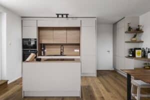 Inselküche „Silbermond“ mit grifflosen Fronten in Beige, Taupe, Kaschmir oder Hellgrau, rustikale Holzoptik bei Arbeitsflächen und Innenleben, Schrankerweiterungen mit Anrichte für zusätzlichen Stauraum und integrierter Essgruppe von DANKÜCHEN.