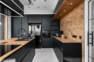 Inselküche „Silbermond“ mit schwarzen grifflosen Fronten, integriertem Rollladenschrank, Arbeitsflächen und Rückwänden in Holzoptik, einem modernen Dunstabzug und Deckenspots von DANKÜCHEN.