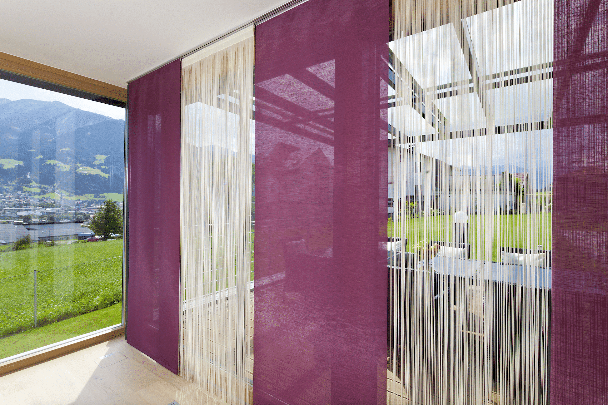Wohnzimmer mit fuchsie-farbenen Flächen- und weißen Fadenvorhängen von DolenzGollner Sonnenschutztechnik Ing. Wagner GmbH.
