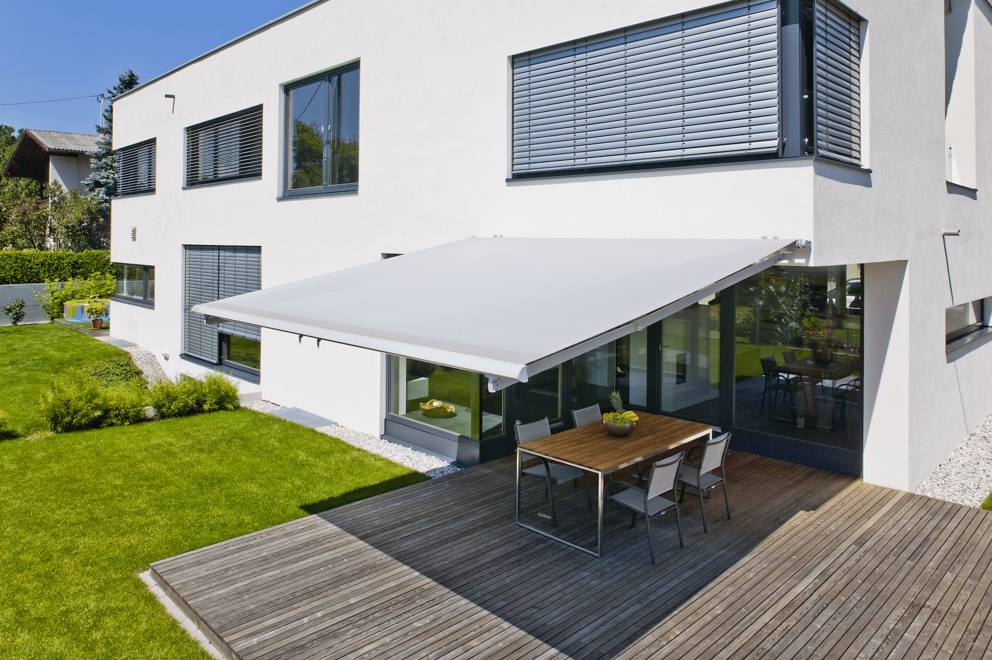 Freundliches Wohnhaus mit ausfahrbarer Markise über dem Essbereich der Holzterrasse von DolenzGollner Sonnenschutztechnik Ing. Wagner GmbH.