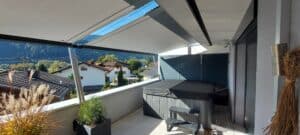 Halbüberdachte Dachterrasse eines Wohnhauses mit fassadenmontiertem Sonnensegel schräg zur Brüstung verlaufend von DolenzGollner.