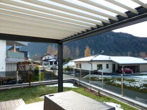 Anbaupergola mit dunklem Alurahmen und einem weissen, gekippten Lamellen von DolenzGollner.