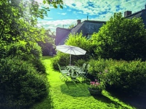 Ein üppiger Garten mit einem freistehenden geneigten Alu-Sonnenschirm in Hellgrau von DolenzGollner.
