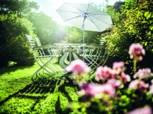 Privatgarten mit Hecken, Rosen, einer romantischen gußeisernen Gartengarnitur und einem freistehenden, geneigten Alu-Sonnenschirm von DolenzGollner.